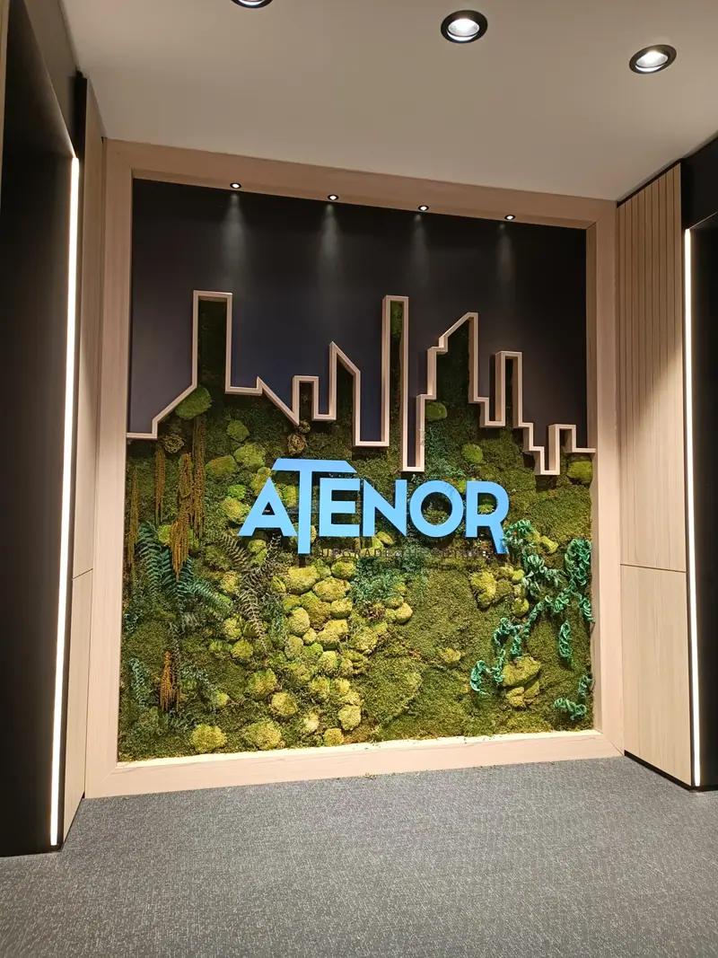 Logo Atenor en grandes lettres bleues sur un mur végétal