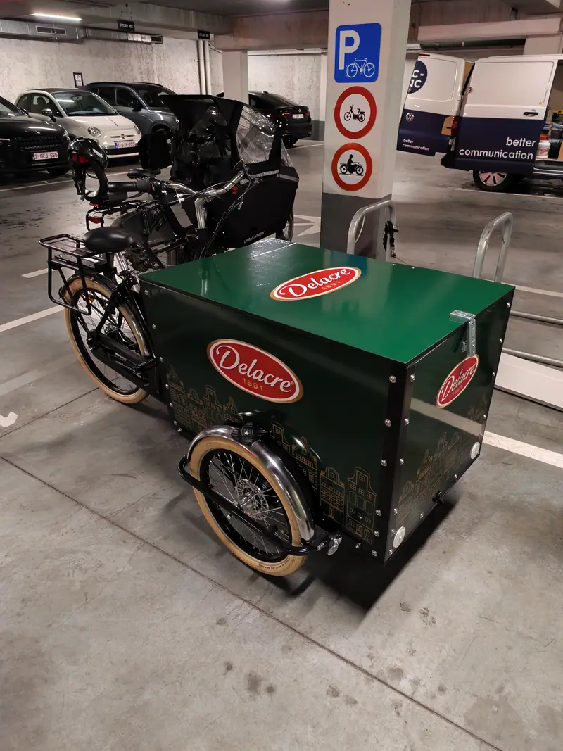 Vélo cargo vert habillé du logo Delacre dans un parking