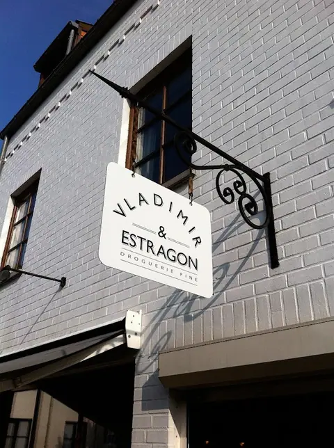Enseigne drapeau Vladimir & Estragon, droguerie fine, sur façade en briques